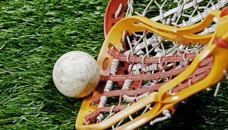 A lacrosse stick scooping up a ball on a green turf field