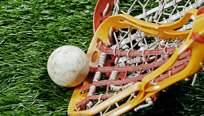 A lacrosse stick scooping up a ball on a green turf field