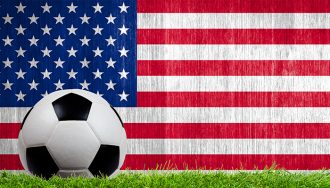 Soccer ball on grass with the American flag in the background