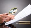 An attorney closely examines a legal document with a magnifying glass.