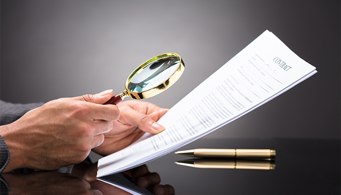 An attorney closely examines a legal document with a magnifying glass.